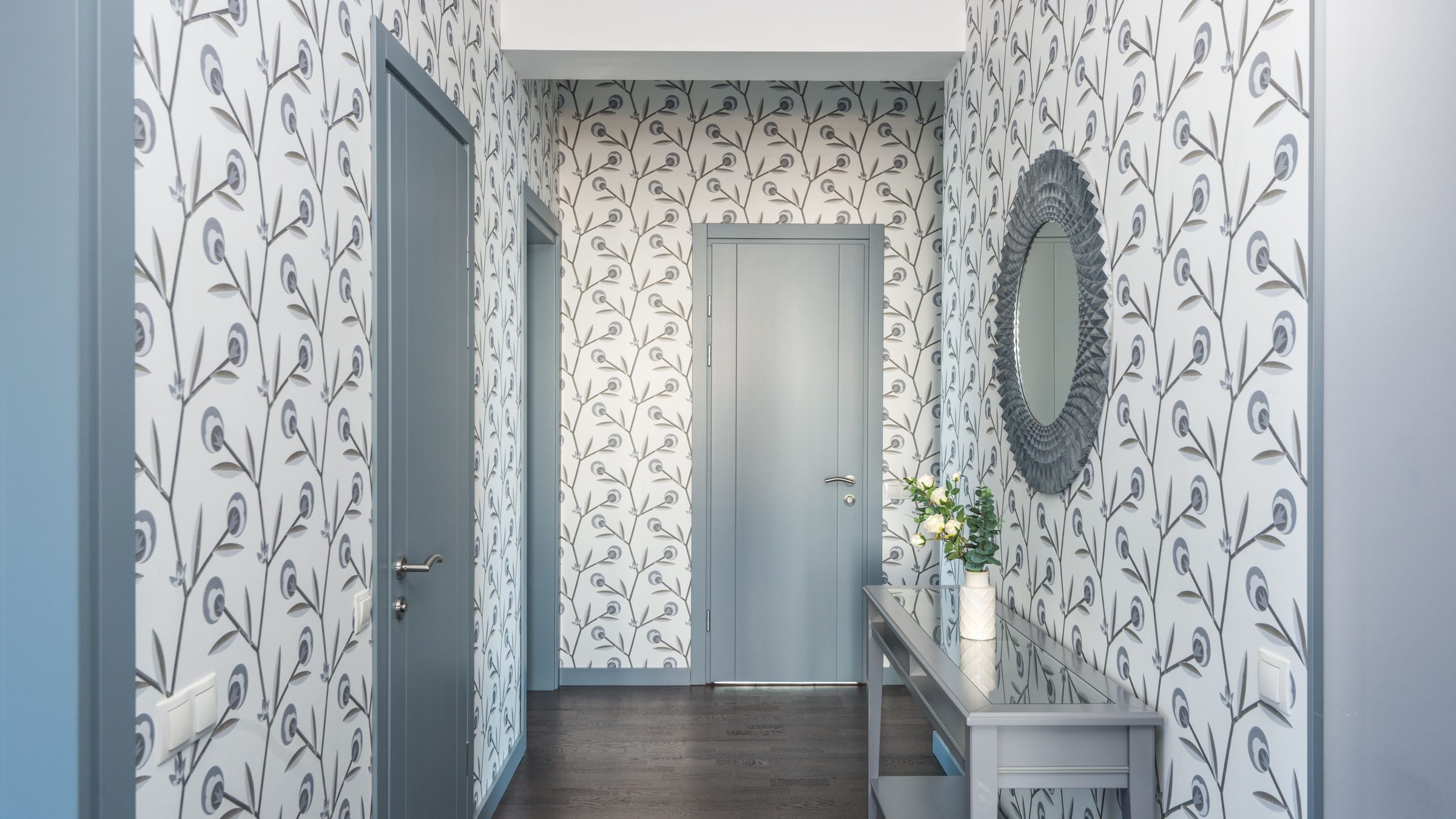 Finished entryway fully papered in a white and grey botanical wallpaper, with a round mirror and a slim console table