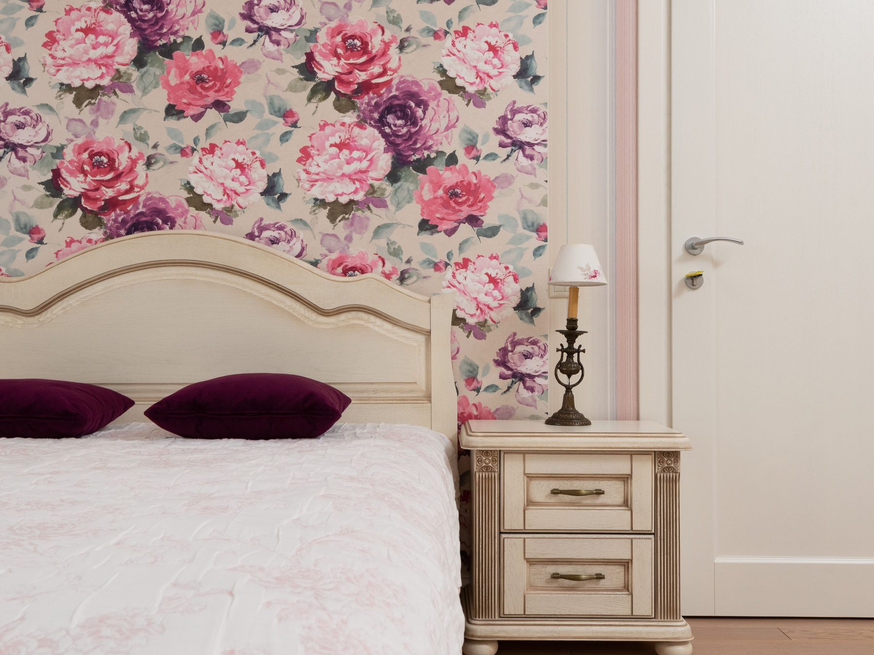 Classic bedroom with a large-scale pink and purple peony wallpaper behind a cream carved headboard