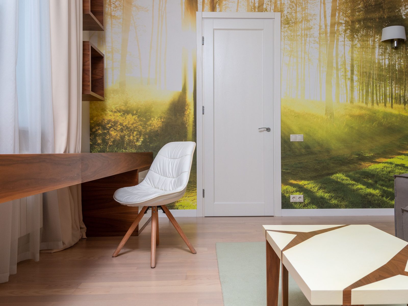 Home office with a full-wall sunlit forest mural wallpaper, a walnut floating desk, and a white chair