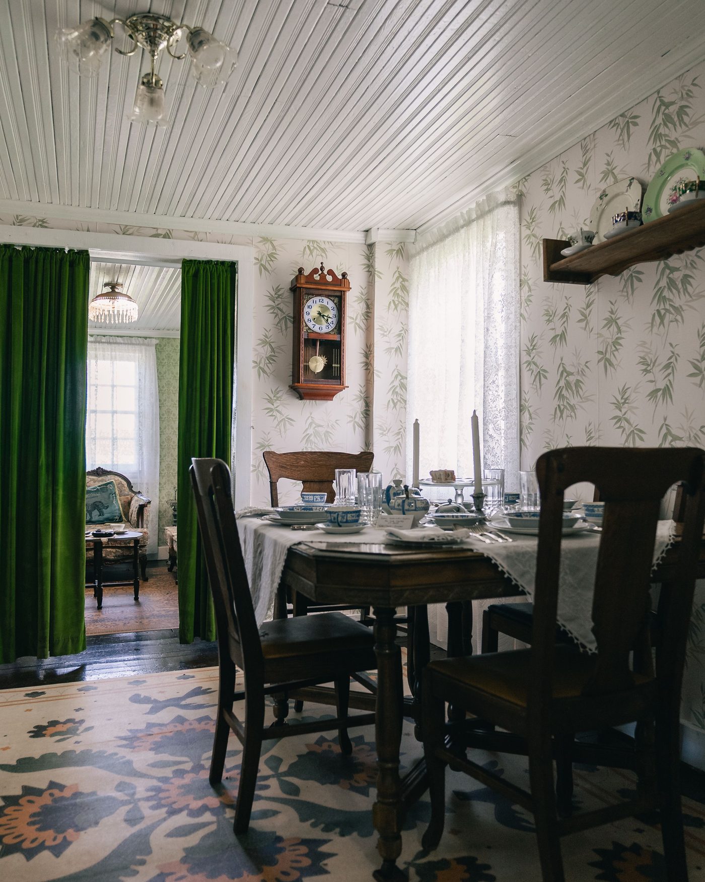 Cottage dining room with white and green leaf-pattern wallpaper, a set wooden table, and green velvet curtains